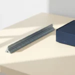 Architectenlineaal diagonaal op wit bureau naast kleine serverunit, geometrische schaduwen in leisteen, marineblauw en ivoor tinten.