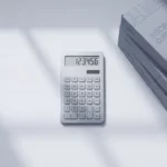 Rekenmachine op wit bureau naast gestapelde Microsoft Office softwareboxen in minimalistisch kantoorinterieur
