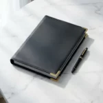 Leren contractmap met gouden sluitingen en vulpen op wit marmeren bureau, bovenaanzicht met natuurlijk licht