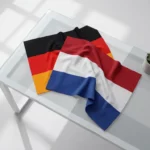Duitse en Nederlandse vlaggen elegant gerangschikt op glazen bureau in minimalistische kantooromgeving met zachte schaduwen