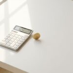 Gouden munt balanceert op rand naast rekenmachine met financiële cijfers op witte minimalistische bureau
