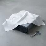 IBM-servers gedeeltelijk in wolkvormig wit doek gewikkeld, met een schaar ernaast op betonnen ondergrond, symboliseert kostenreductie na cloudmigratie.