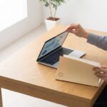 Professionele handen sluiten laptop met procurement grafieken naast manila map op houten bureau in kantoor