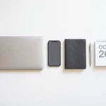 Wit bureau met laptop, smartphone, leren notitieboek, zilveren pen en kalender in geometrische opstelling met zachte schaduwen