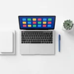 Wit bureau met laptop met kleurrijke app-iconen, blauwe pen en kleine vetplant in minimalistische opstelling