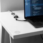 Laptop met code op scherm op minimalistische witte bureau met kabelmanagement en zachte natuurlijke verlichting