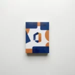 Microsoft Office softwarebox in marineblauw en oranje op wit bureau met zachte schaduwen, bovenaanzicht