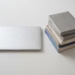 Zilveren laptop naast stapel gebruikte Microsoft Office softwareboxen op wit bureau met minimalistische opstelling