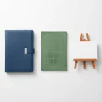 Microsoft Office applicaties weergegeven als elegante fysieke objecten op wit bureau: blauwe map, groene spreadsheet en oranje presentatie-ezel