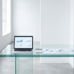 Glazen bureau met laptop die financiële grafieken toont, calculator en documenten in moderne witte kantooromgeving