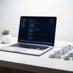Moderne laptop met code op scherm op witte werkplek met geometrische accessoires en kleine vetplant