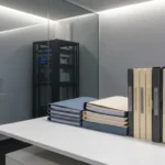 Nette stapel compliance-mappen en documentatiebinders op wit bureau, met IBM-serverrack zichtbaar door glazen wand op de achtergrond.