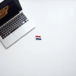 Witte bureau met laptop met SAP-logo en Nederlandse vlag speld, minimalistisch bovenaanzicht