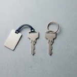 Twee identieke metalen sleutels op betonnen ondergrond, één met eigendomslabel, één met herhalende ring, strak minimalistisch bovenaanzicht.