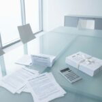 Glazen vergadertafel met softwarelicentiedocumenten, calculator en contracten in minimalistisch kantoor
