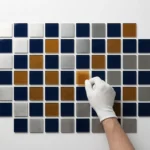 Hand die geometrische tegels in een strak grid rangschikt op wit oppervlak, marineblauw en zilver met één amber accent.