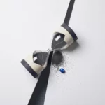 Gebarsten zandloper lekt zand op wit oppervlak, symboliseert oplopende kosten, minimalistische flatlay met blauw accent en geometrische schaduw.